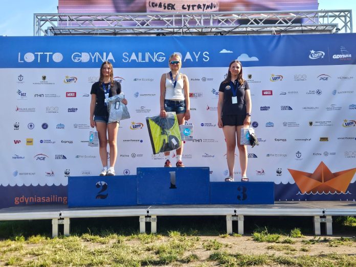 Trzy młode żeglarki na podium mistrzostw Polski w Gdyni, z medalami i nagrodami.